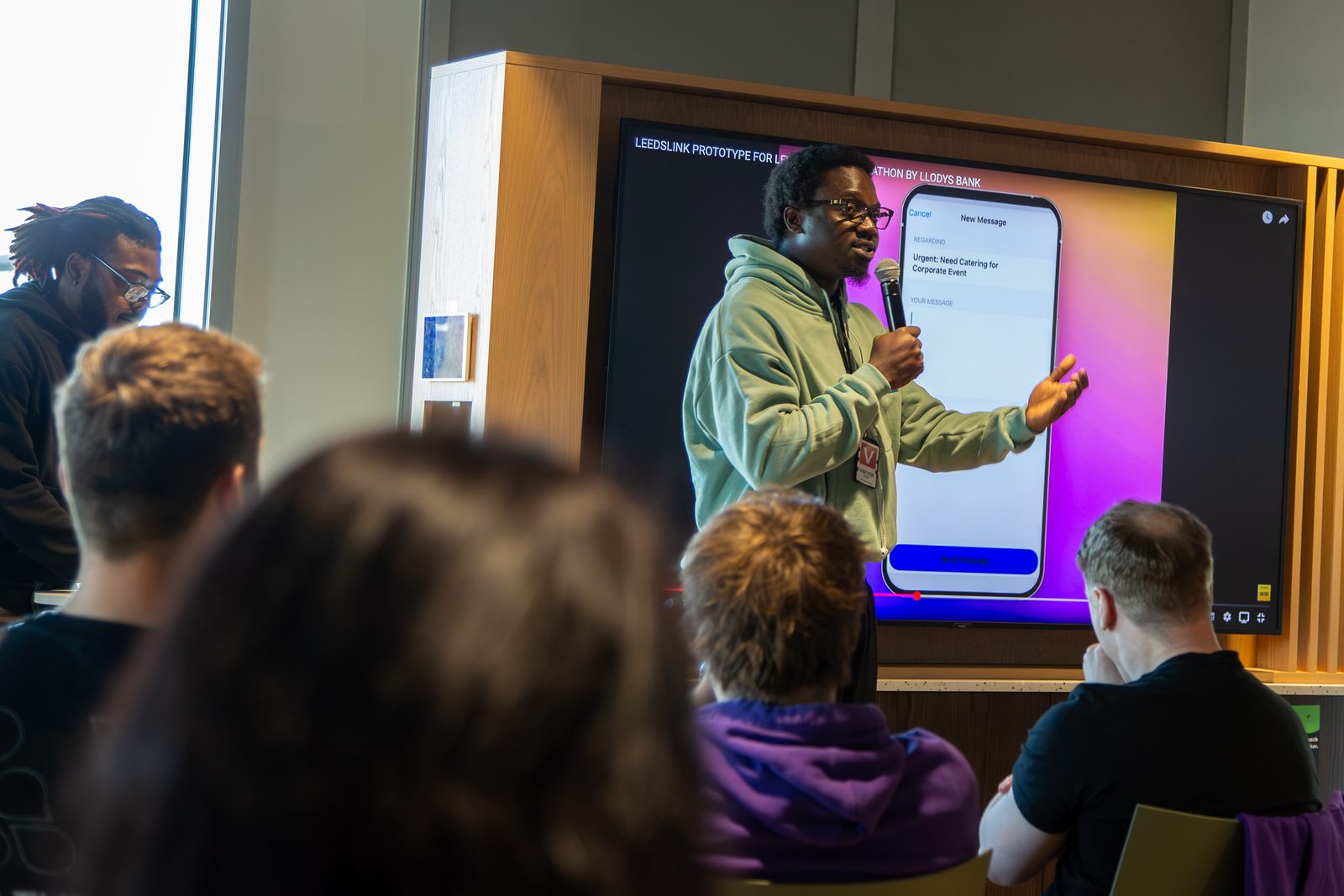 Ikechukwu presenting to a seated audience in front of a slide titled 'LeedsLink prototype for Leeds Digital Hackathon by Lloyds Bank'